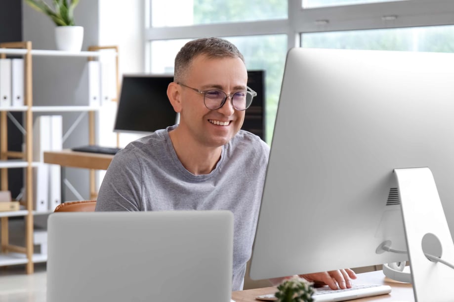 Répartiteur souriant travaillant sur ordinateur dans son bureau, optimisant les itinéraires et la répartition des camions lourds avec Neo TMS.