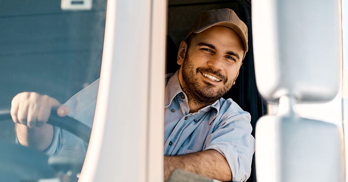 Chauffeur de camion souriant vu depuis sa cabine. Neo Paie des chauffeurs automatise le calcul des salaires grâce aux données de télémétrie, réduit les tâches administratives et augmente la satisfaction de vos équipes.